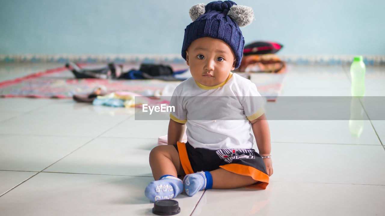 Portrait of cute boy sitting on tiled floor