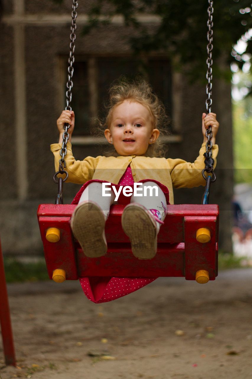 Portrait of girl sitting on swing at playground