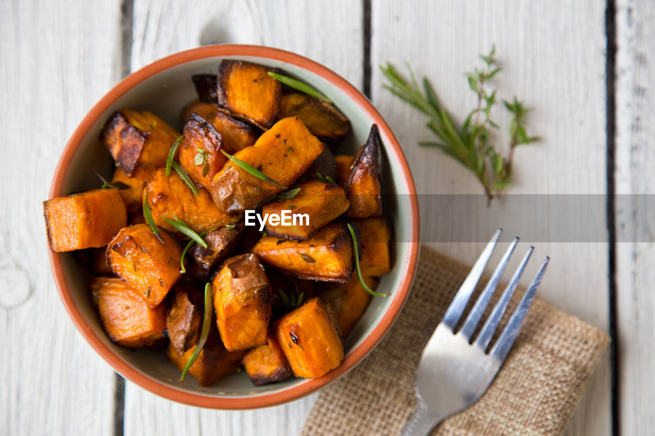 High-angle view of bowl of oven roasted sweet potato cubes with fresh herbs