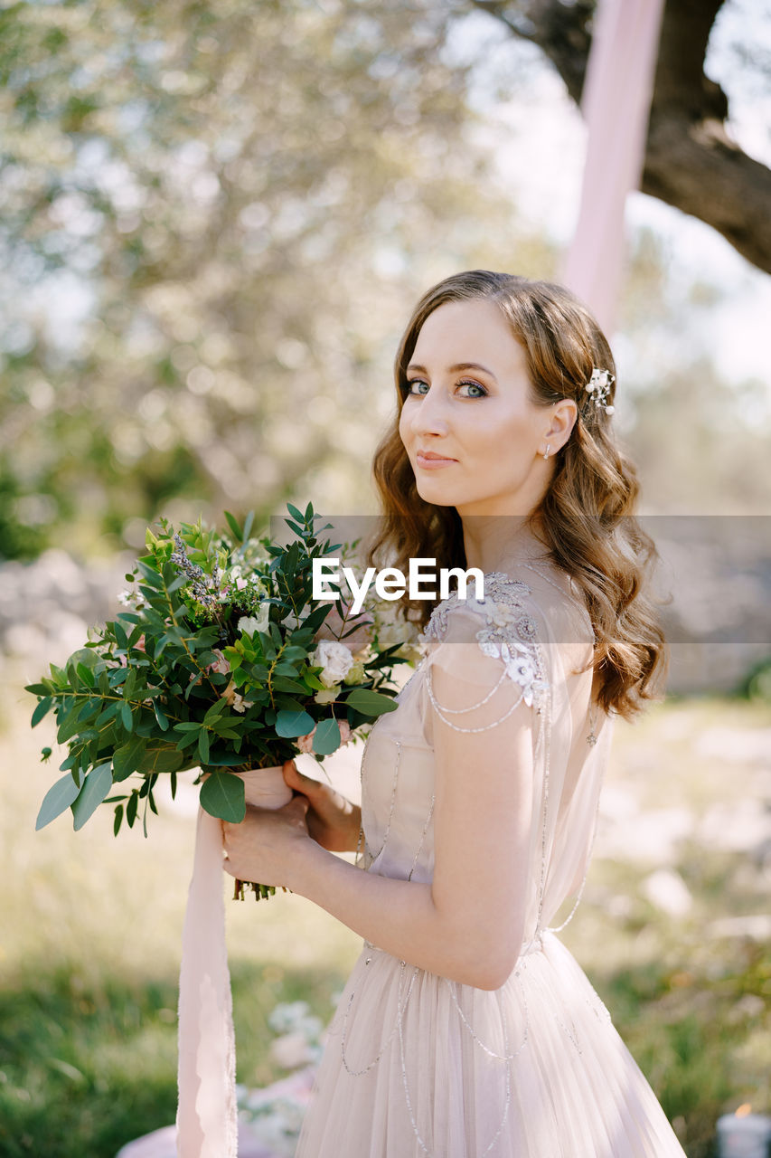 Portrait of young woman standing against plants