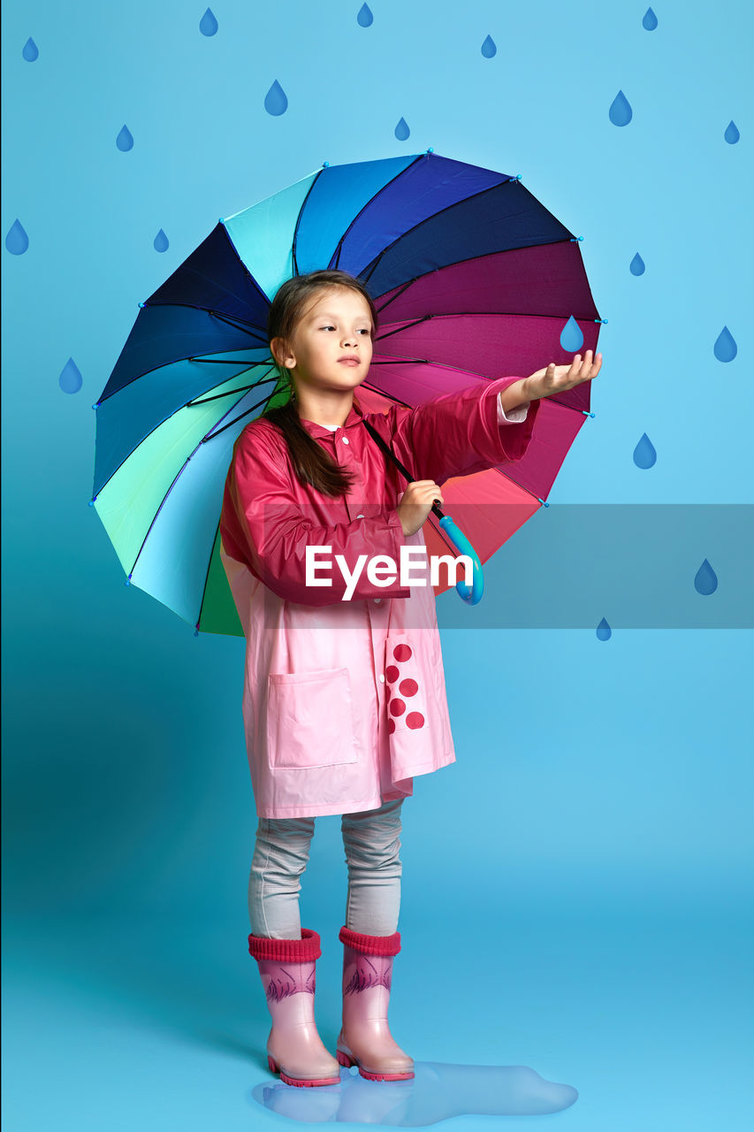 full length of woman with umbrella against blue background