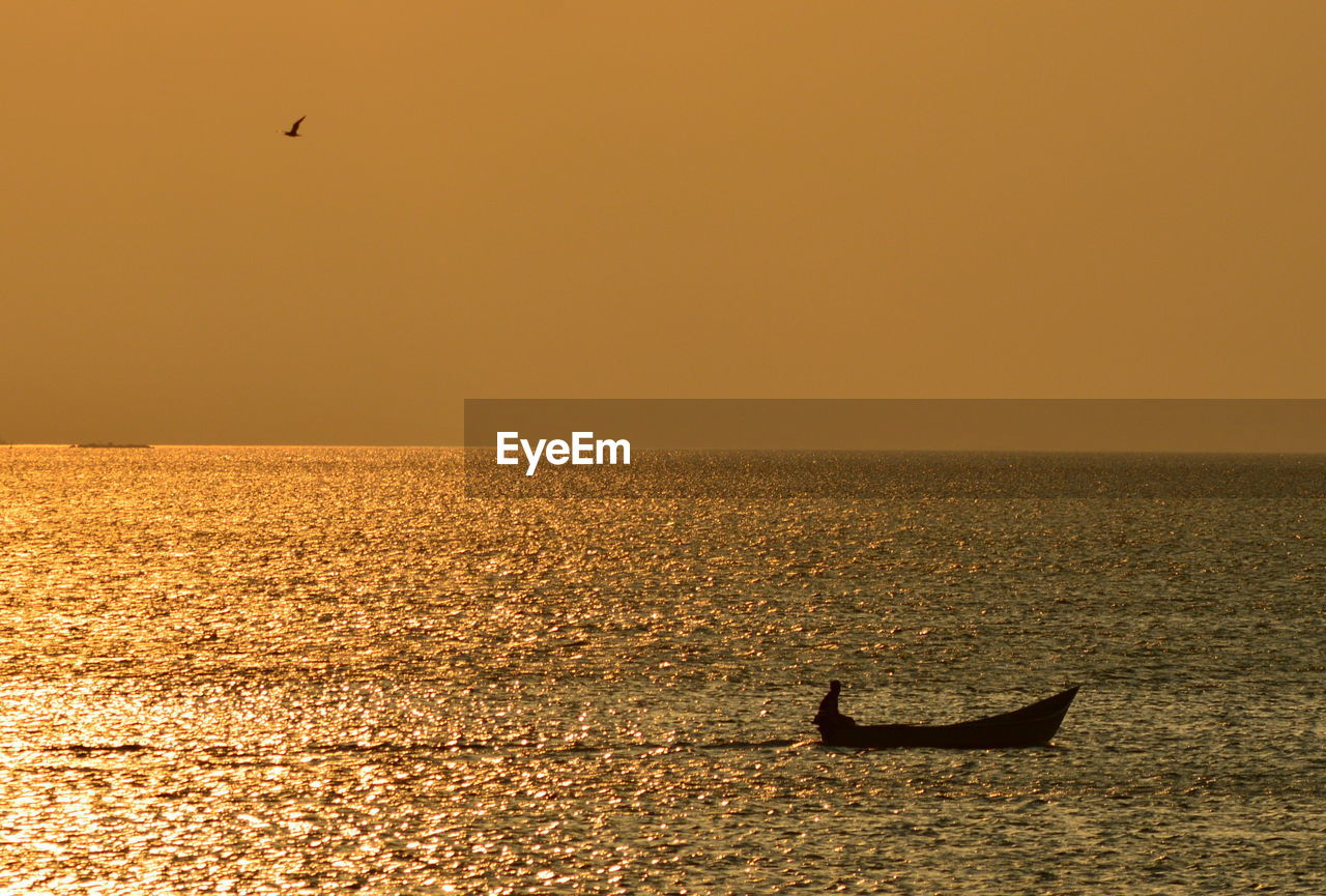 Silhouette boat moored on sea against clear sky during sunset