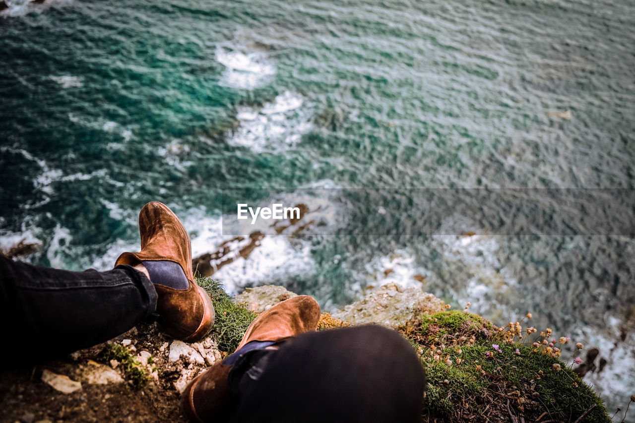 Low section of man sitting by sea