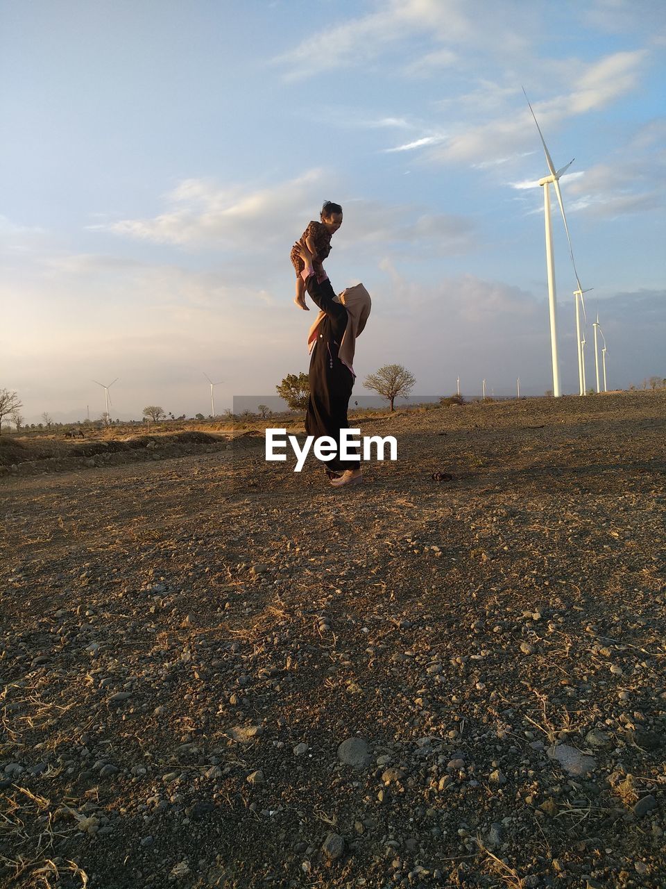 Mother picking up son while standing on land against sky