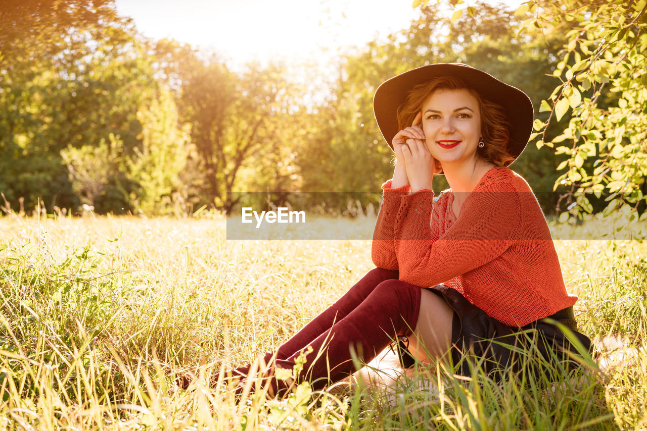 PORTRAIT OF SMILING YOUNG WOMAN SITTING ON GRASS