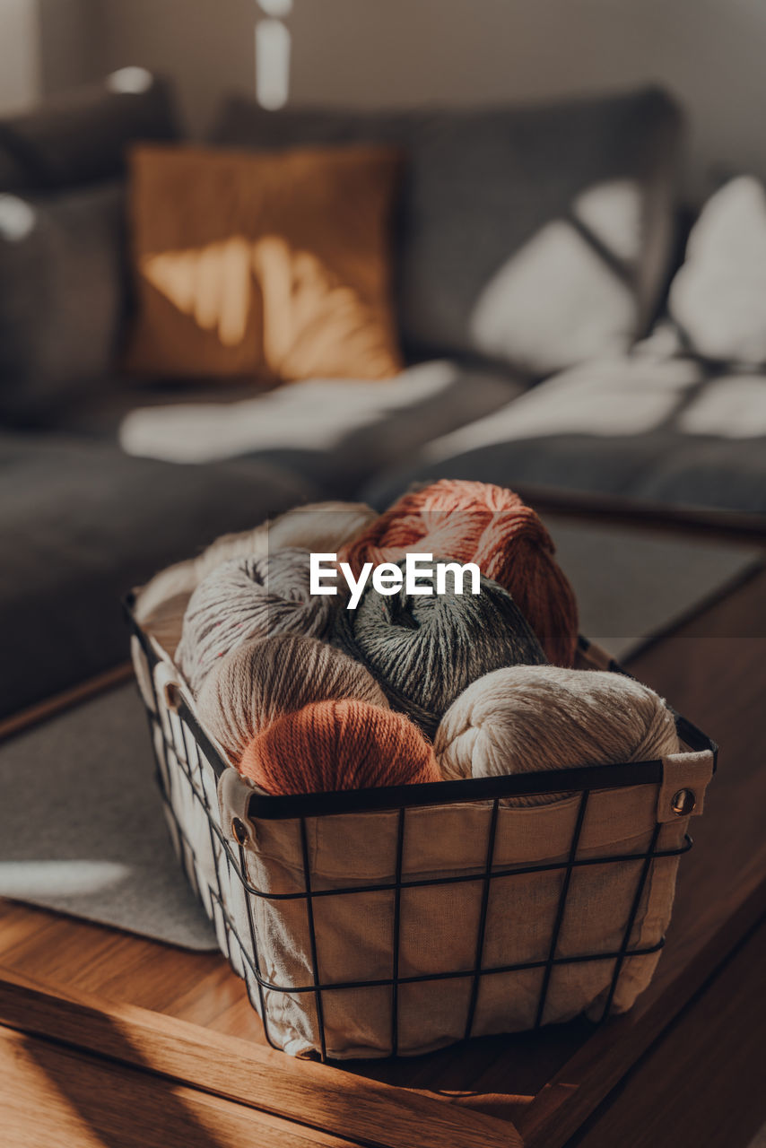 Balls of earth coloured yarn inside a basket on a table inside an apartment.