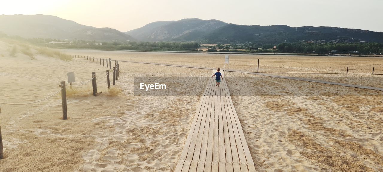 Little boy walking on wooden pathway on sand beach