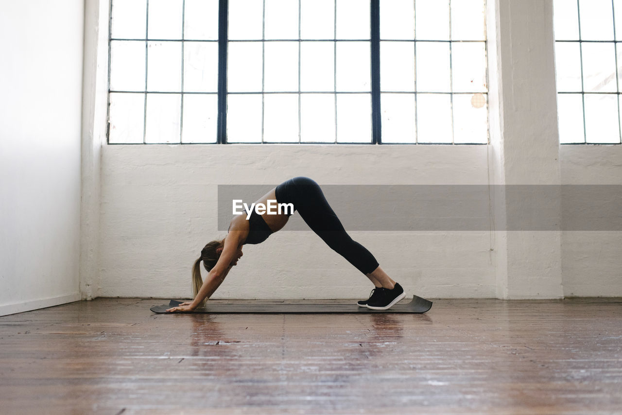 Side view of female athlete practicing downward facing dog position in gym