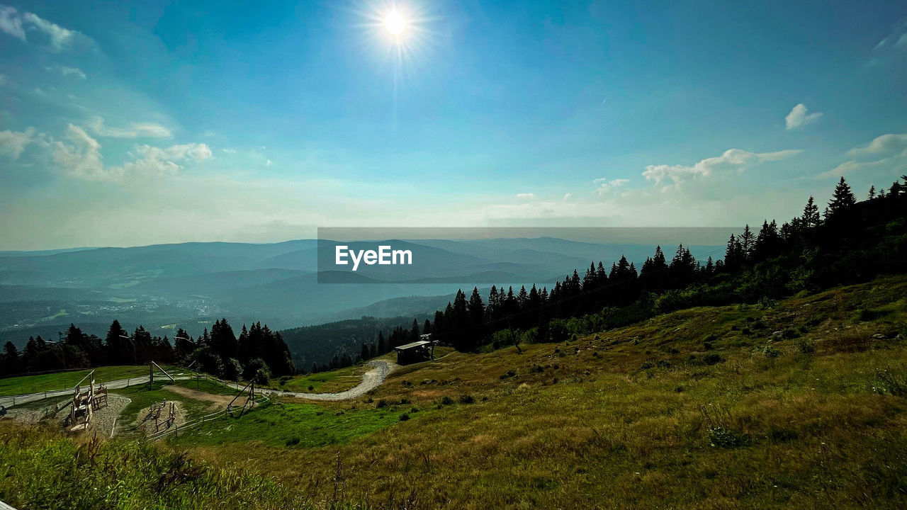 sky, environment, nature, landscape, mountain, scenics - nature, mountain range, plant, beauty in nature, land, cloud, tree, tranquility, morning, sun, tranquil scene, grass, forest, wilderness, sunlight, no people, meadow, sunbeam, non-urban scene, panoramic, plateau, travel, valley, horizon, travel destinations, green, outdoors, ridge, field, idyllic, blue, lens flare, rural scene, coniferous tree, pine tree, pinaceae, plain, highland, summer
