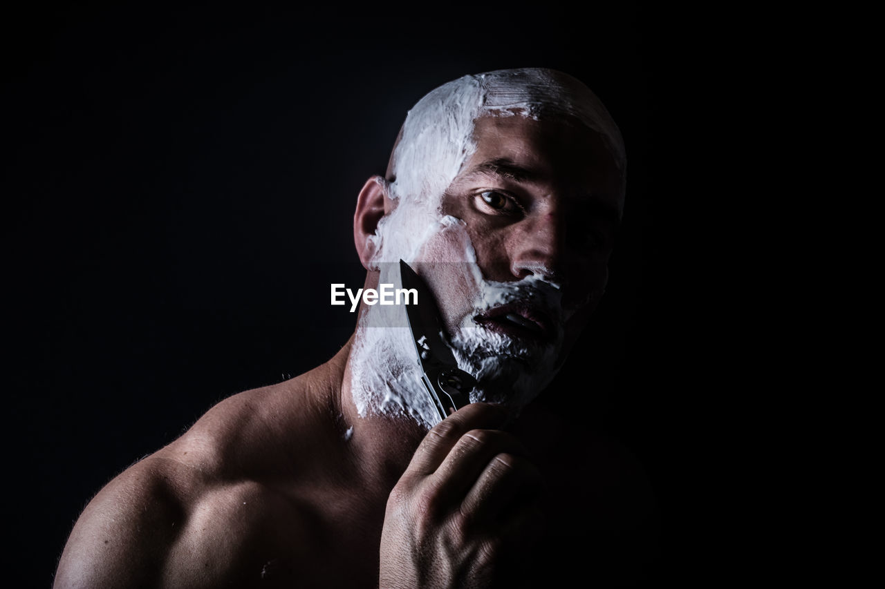 Man shaving with knife against black background