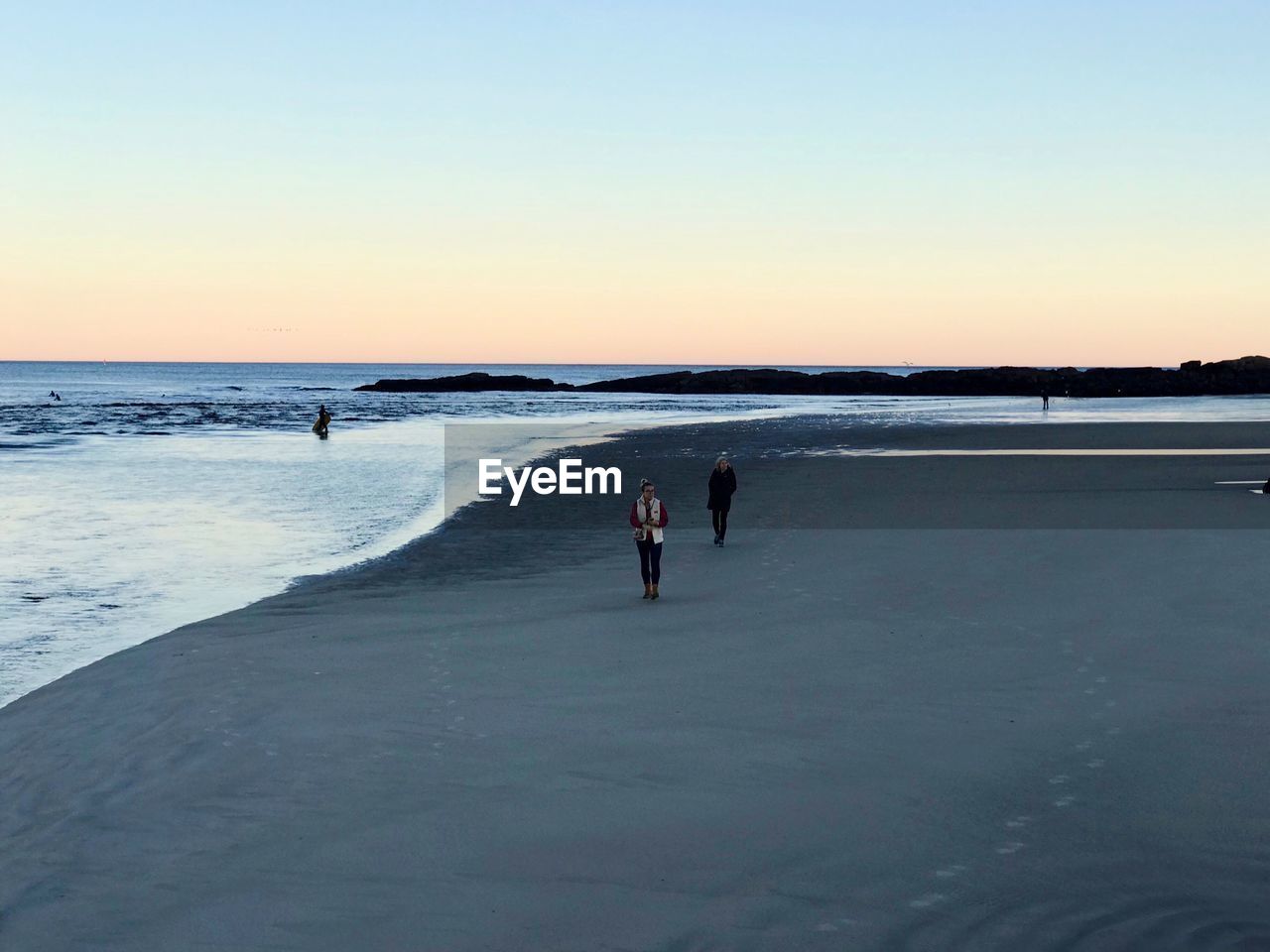 People at beach against clear sky during sunset