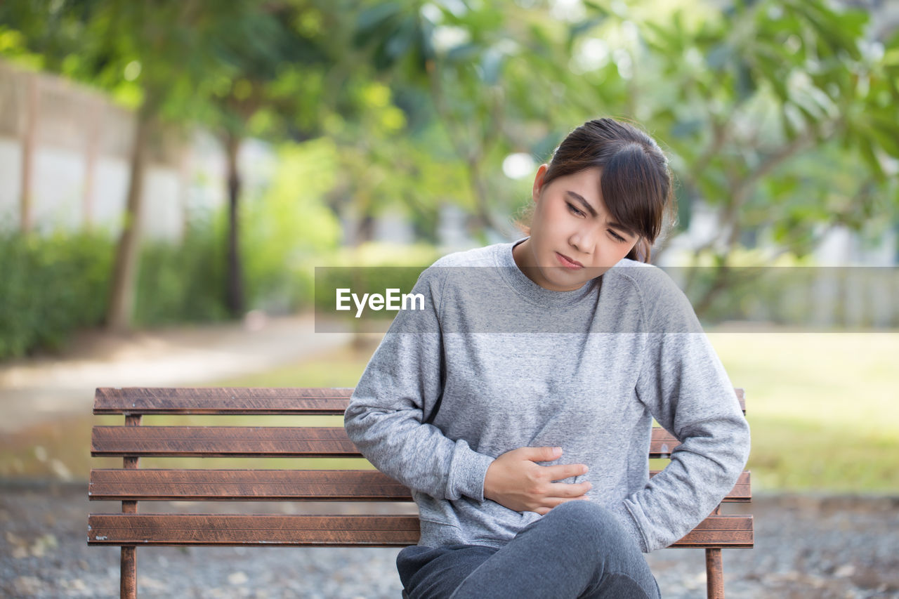 Young woman with stomachache sitting on park bench