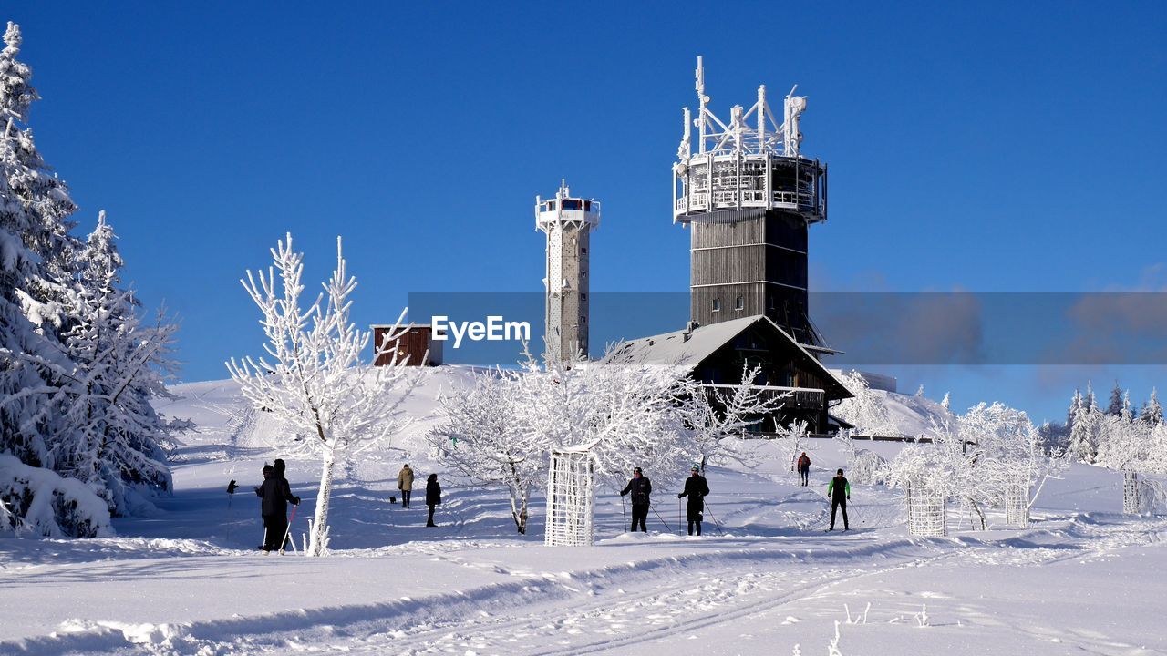 People on snow covered field by towers against sky