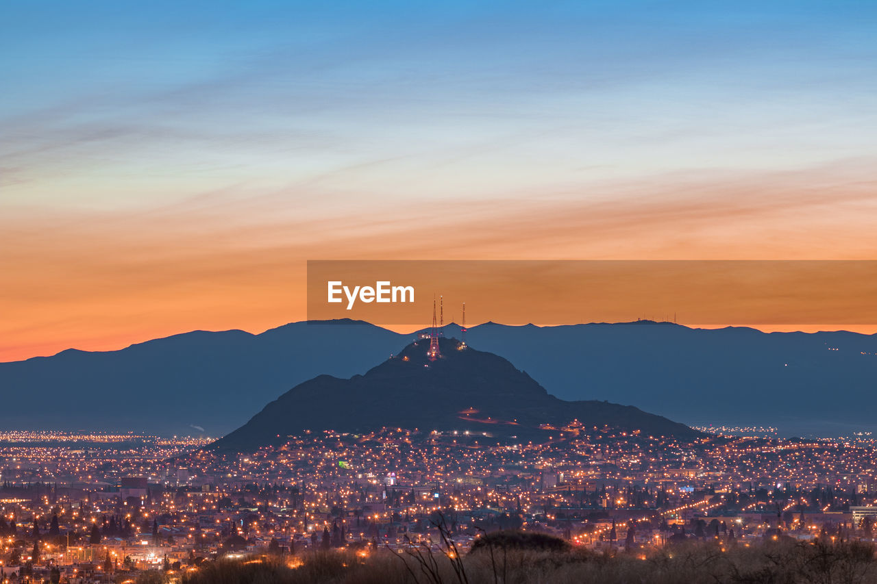 Illuminated cityscape against sky at sunrise