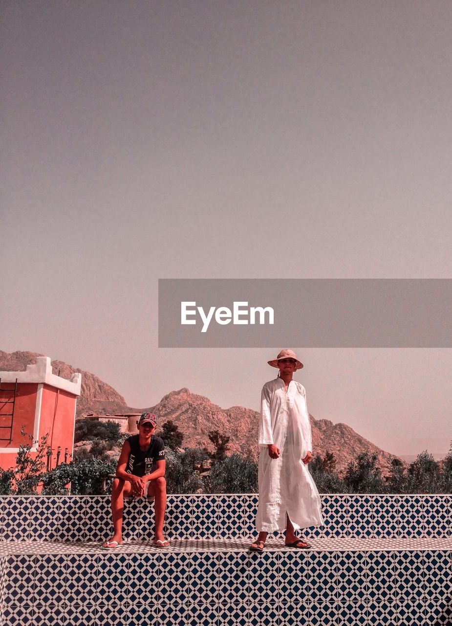 REAR VIEW OF PEOPLE STANDING ON LANDSCAPE AGAINST SKY