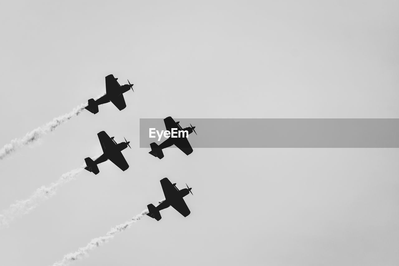 Four aerobatic planes flying in formation in clear sky.