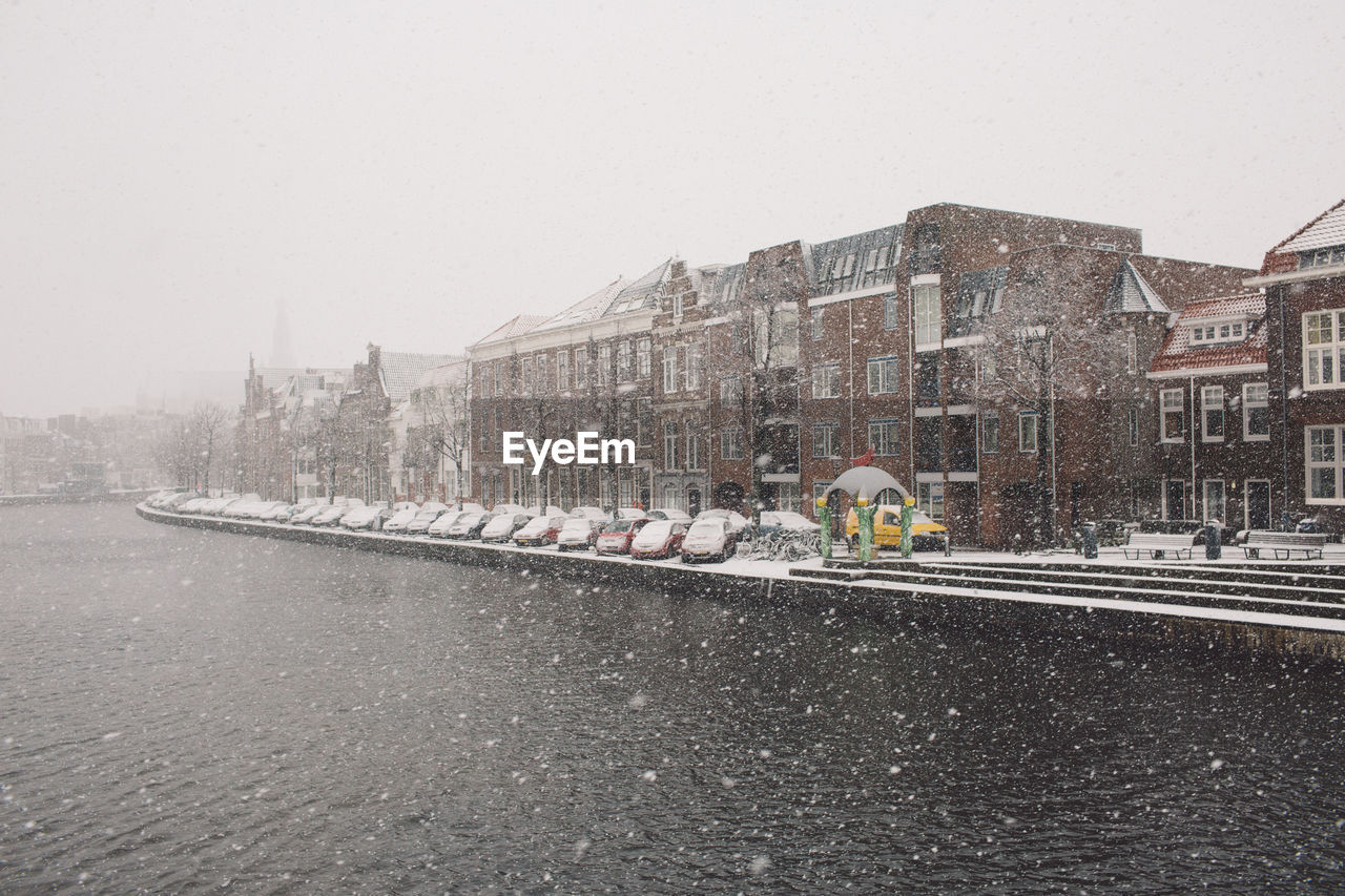 River by buildings against sky during snowfall