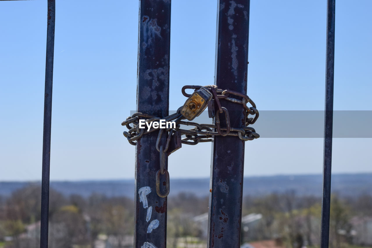 Padlock with chain tied up on gate against clear sky