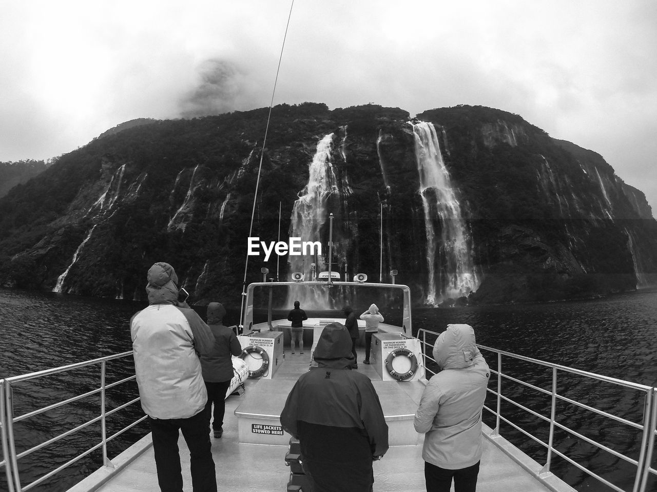 Rear view of people standing on ship in sea against waterfalls