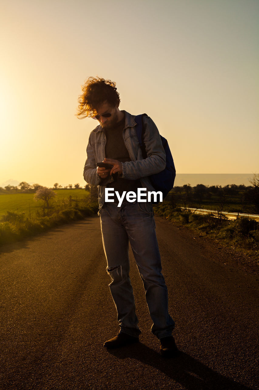 Full length of man standing on road against sky during sunset