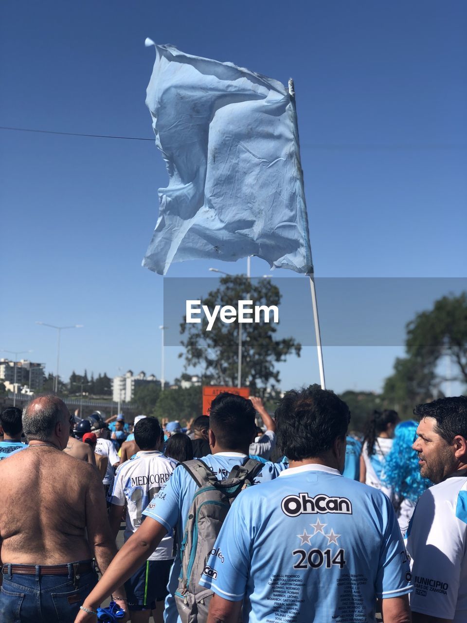 REAR VIEW OF PEOPLE STANDING AGAINST BLUE SKY