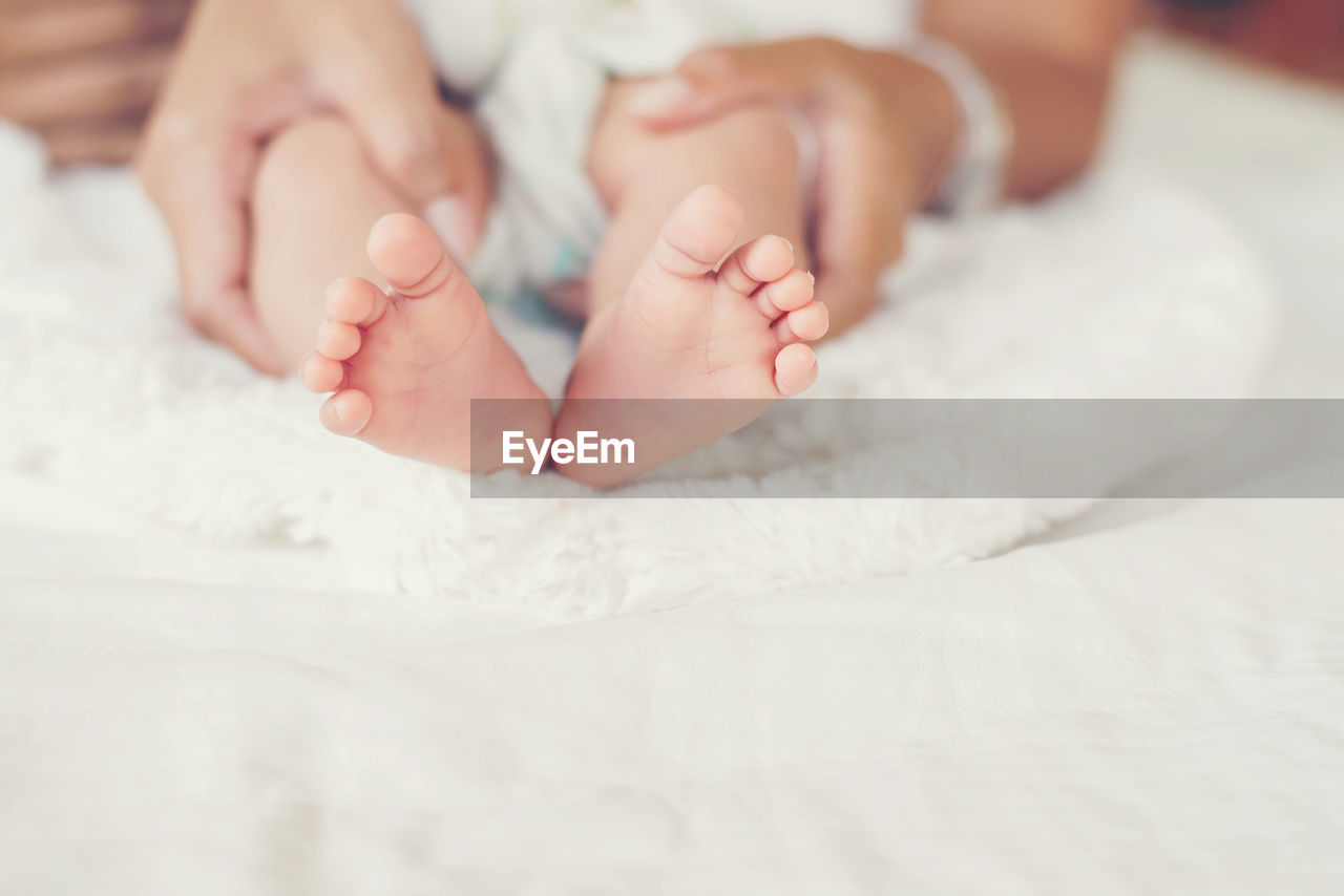 Cropped hands of mother holding baby feet on bed