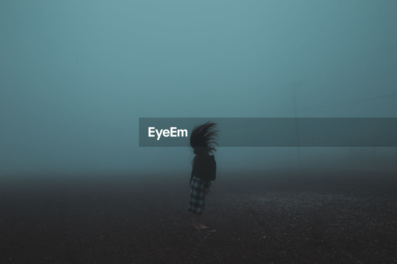 Side view of woman tossing hair while standing on field during foggy weather