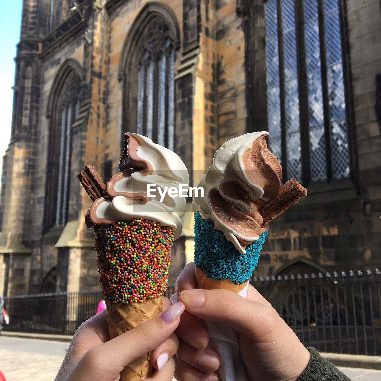 Cropped hands of friends holding ice cream cone against historic building