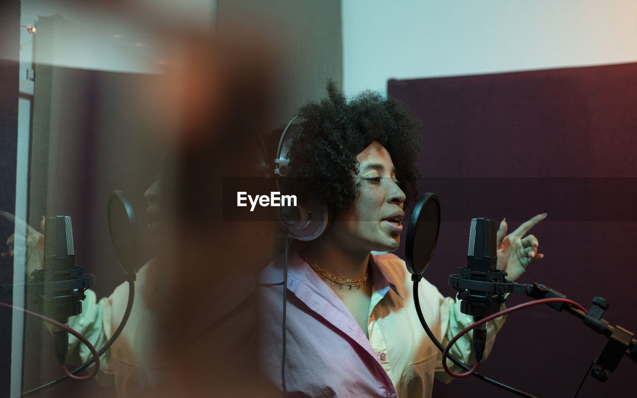 Black female singer performing song against microphone with pop filter while standing and looking forward in sound studio