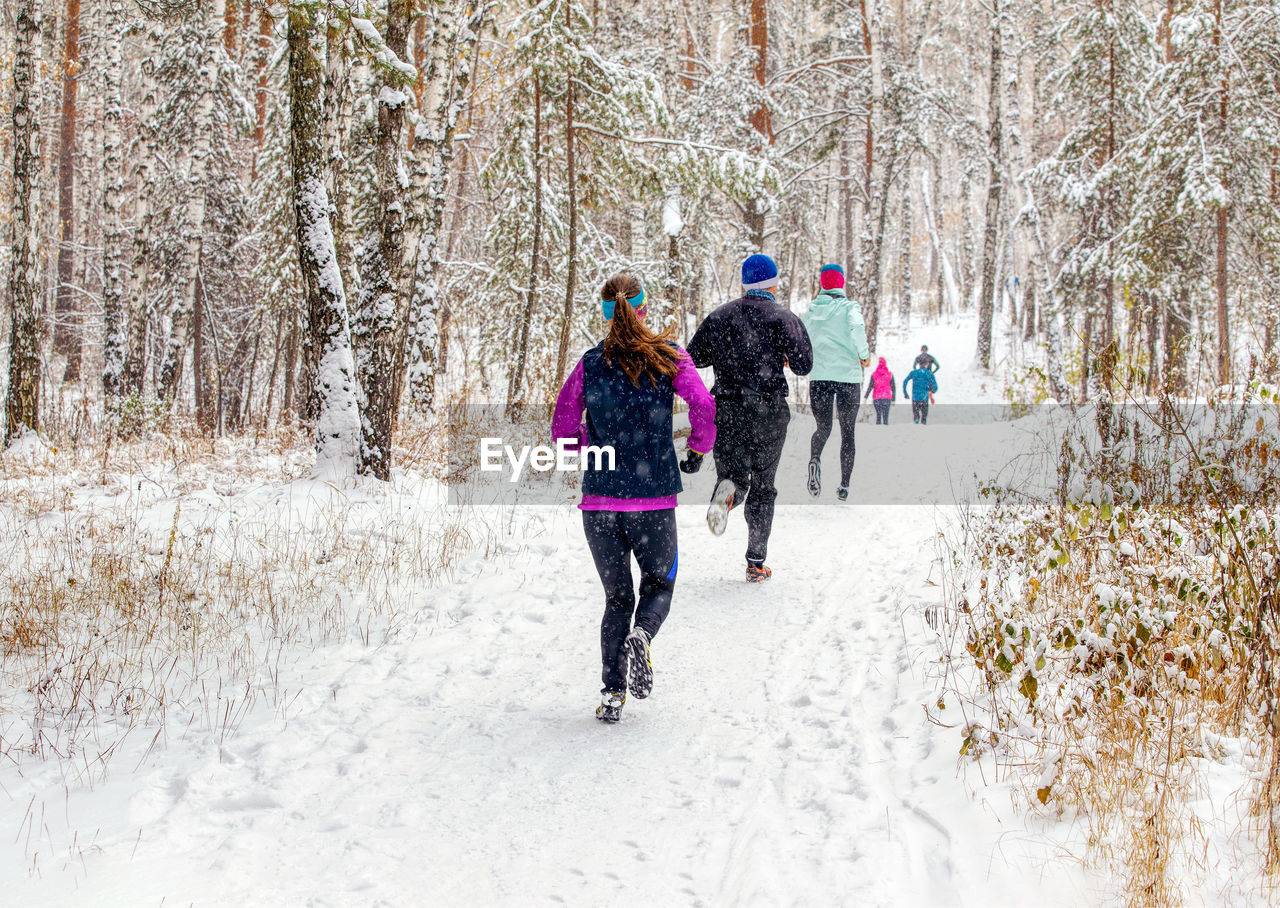 Back group runners run winter trail race in forest during a snowfall