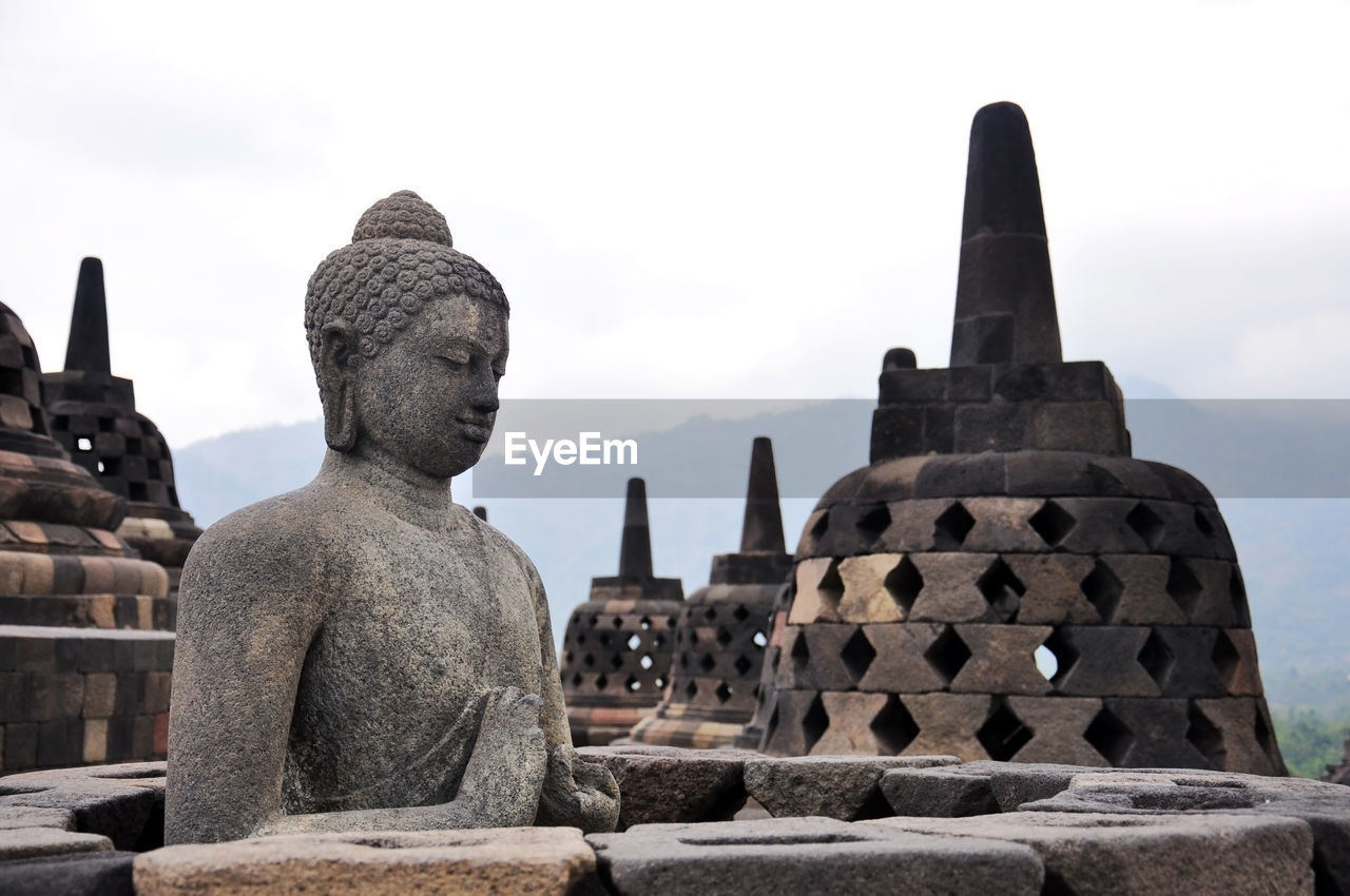 Buddha statue and stupas at borobudur against sky