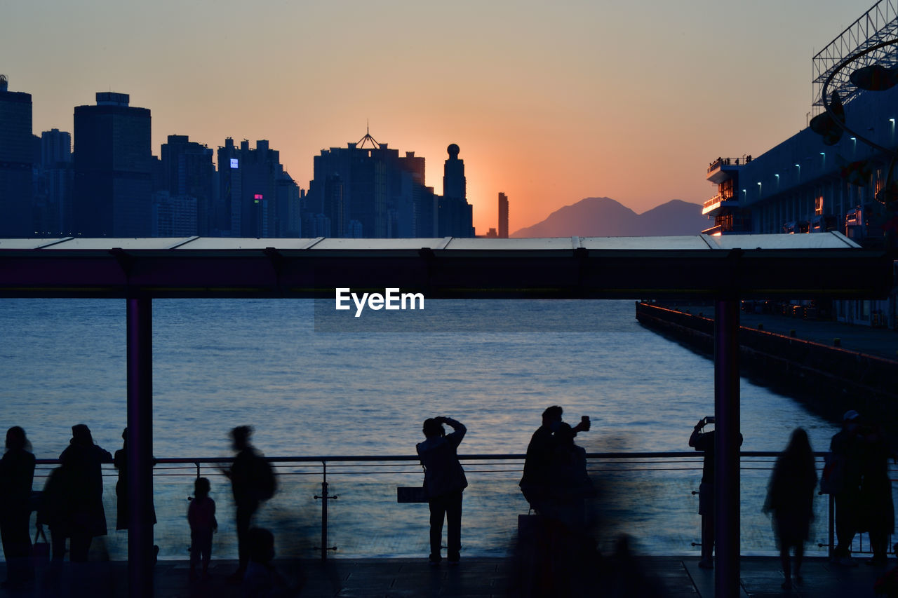 Silhouette people by sea against sky during sunset