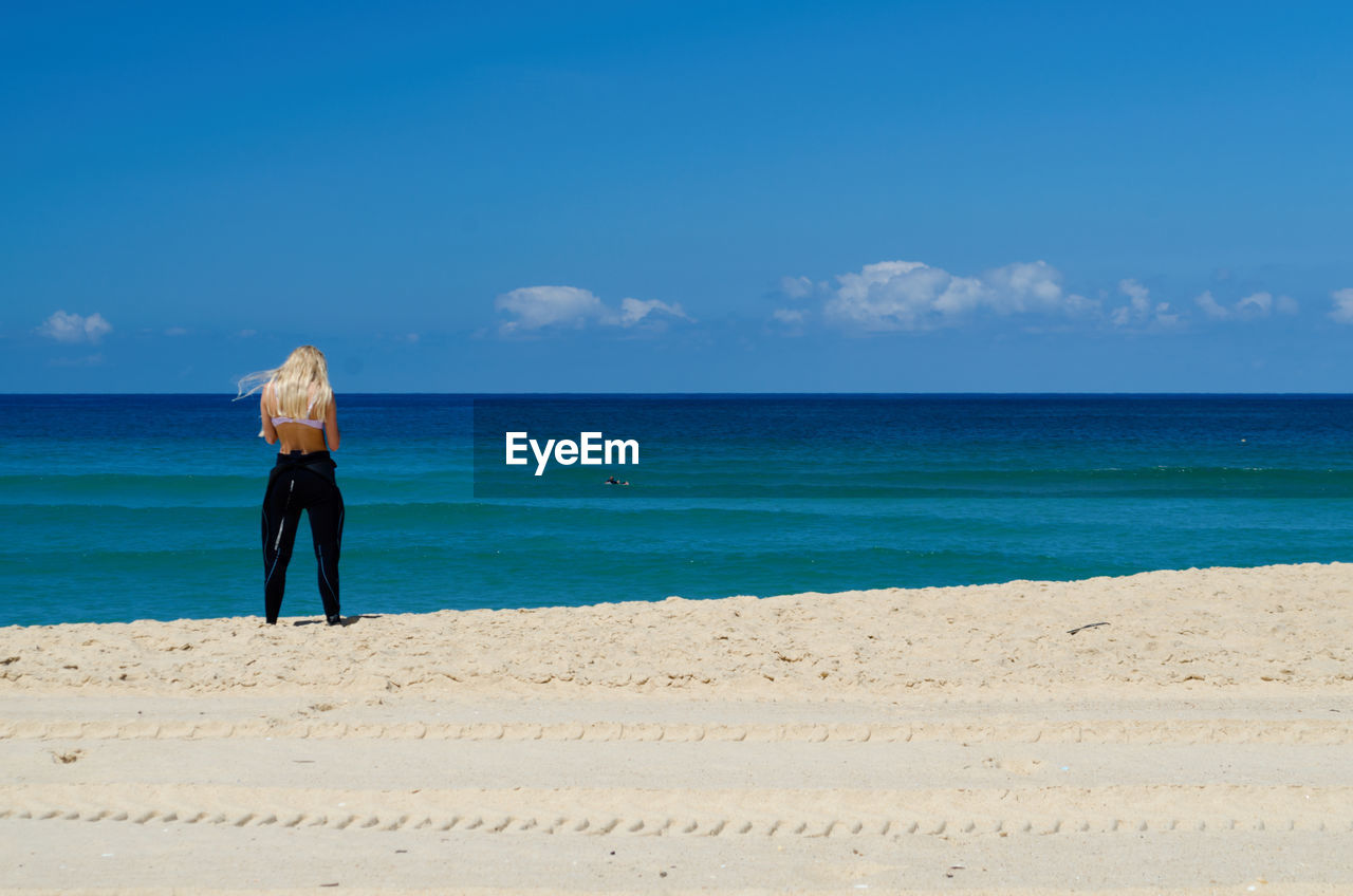 Rear view of woman standing on sand at beach against blue sky