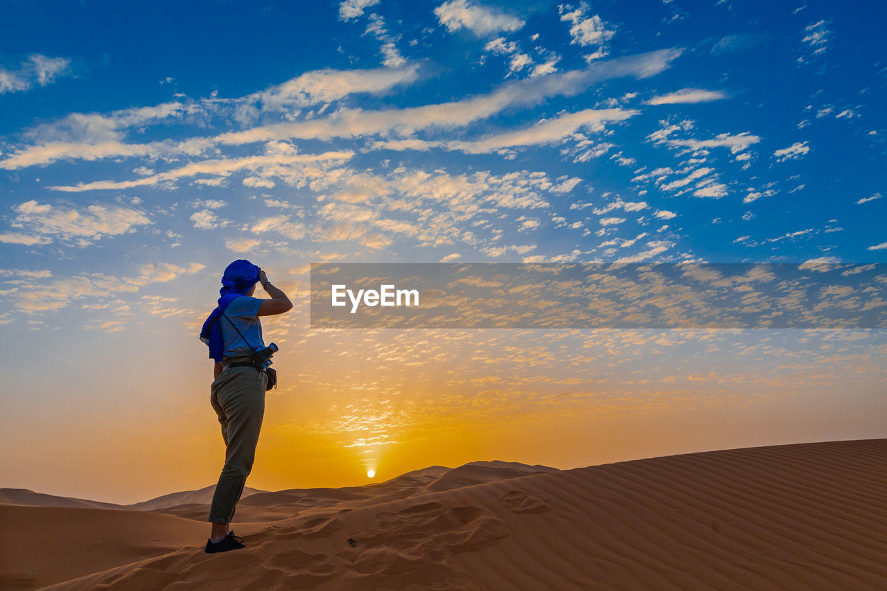 Man standing in desert against sky during sunset