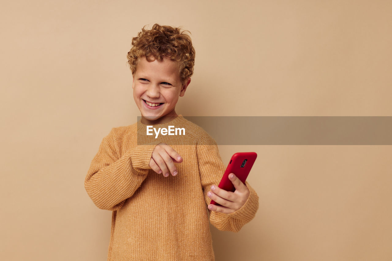 Boy holding smart phone against beige background