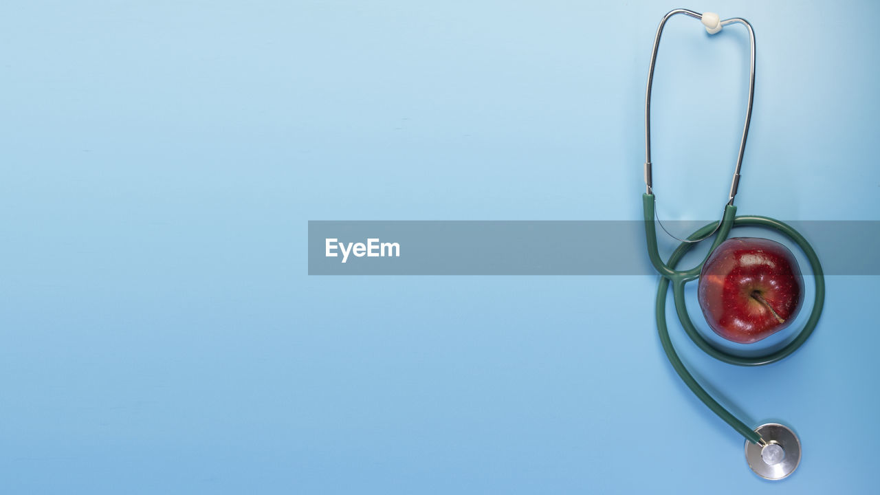 Stethoscopes green silver and a red apple on blue background and writing space.