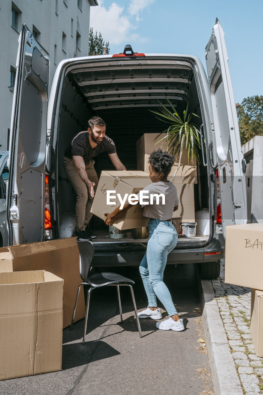 Multiracial couple unloading cardboard boxes from van trunk