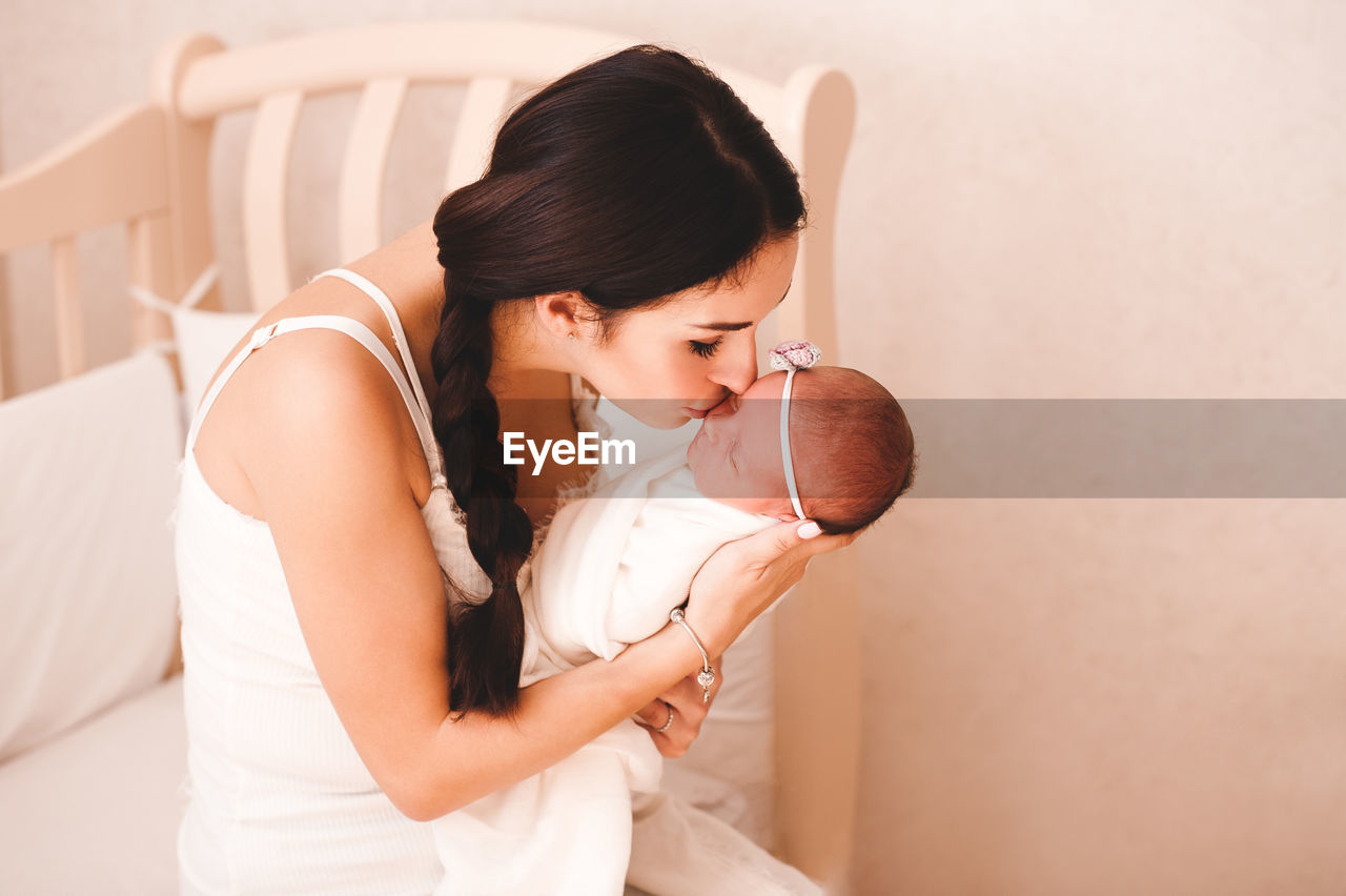 Mother kissing newborn daughter at home