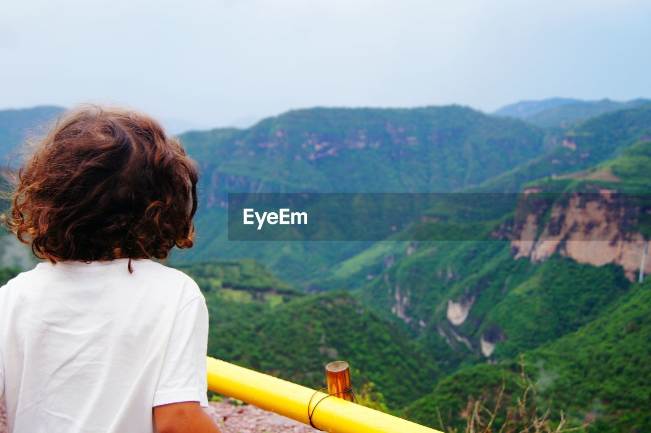 Rear view of boy looking at mountain against clear sky