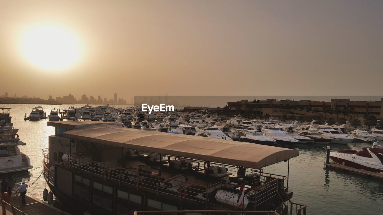 Boats moored in harbor at sunset