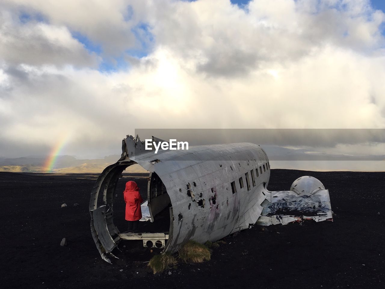 Rear view of woman standing in crashed airplane on field against cloudy sky