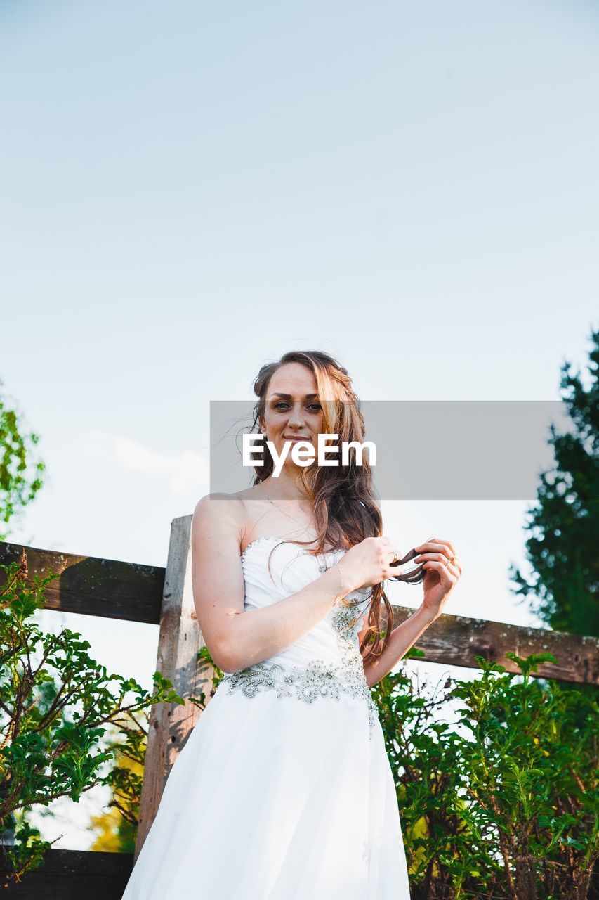 Portrait of smiling young woman standing against sky