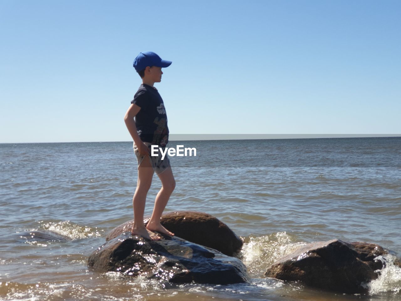 Full length of man on rock at beach against clear sky