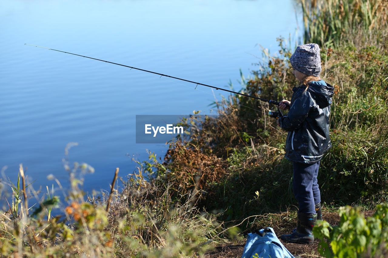 Six year old girl fishing on the autumn lake with a fishing rod