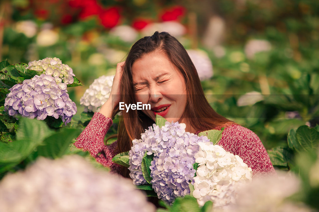 Smiling woman scratching head by flowering plants