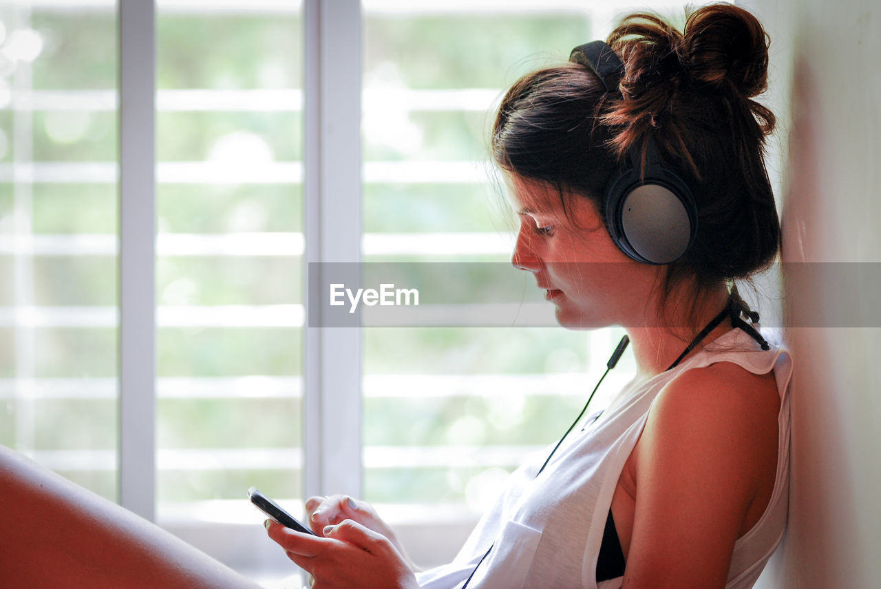 Woman listening music while sitting on window sill