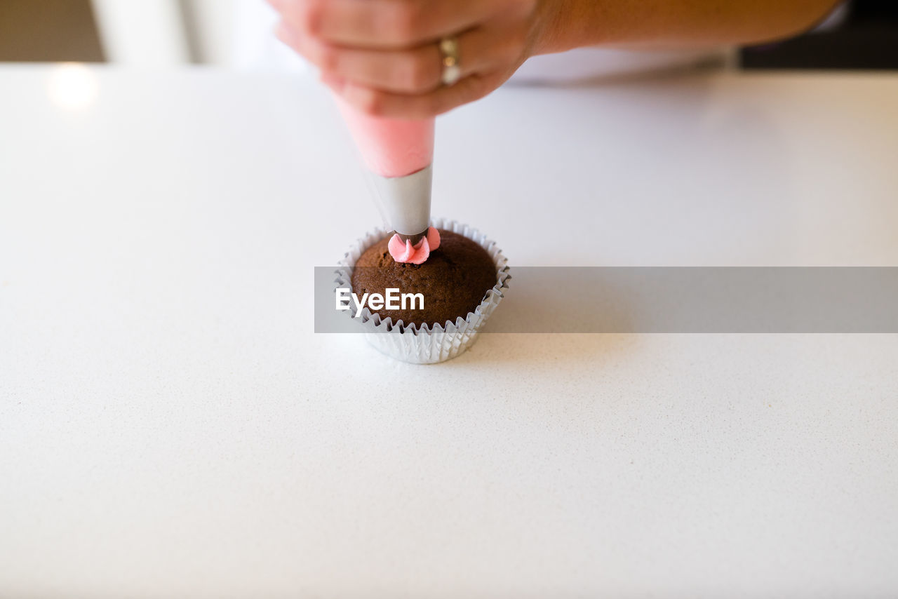 A baker starting to decorate a cupcake with pink frosting