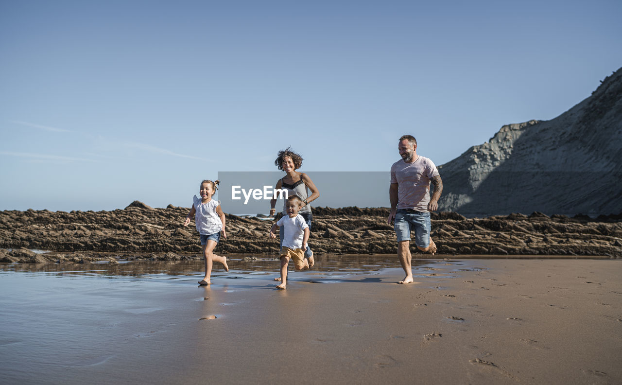 Playful family running at beach against blue sky