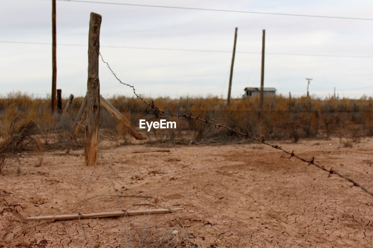 Broken barbed wire on field against sky