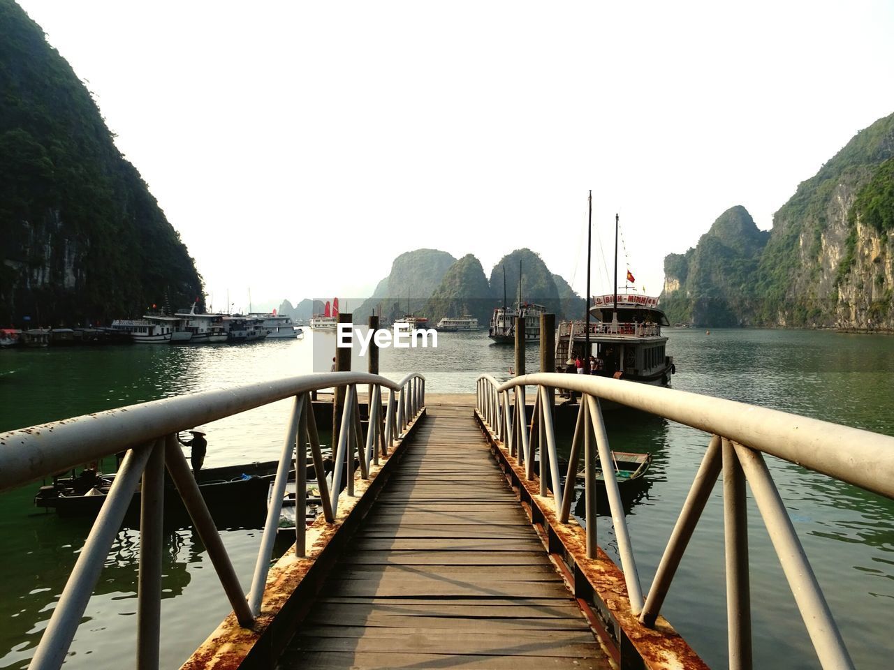 Pier leading towards boats moored on sea against clear sky